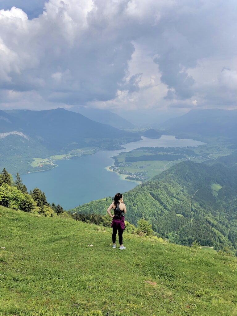 Girl stands in the distance on the crest of a hill, overlooking mountains and a mountain lake