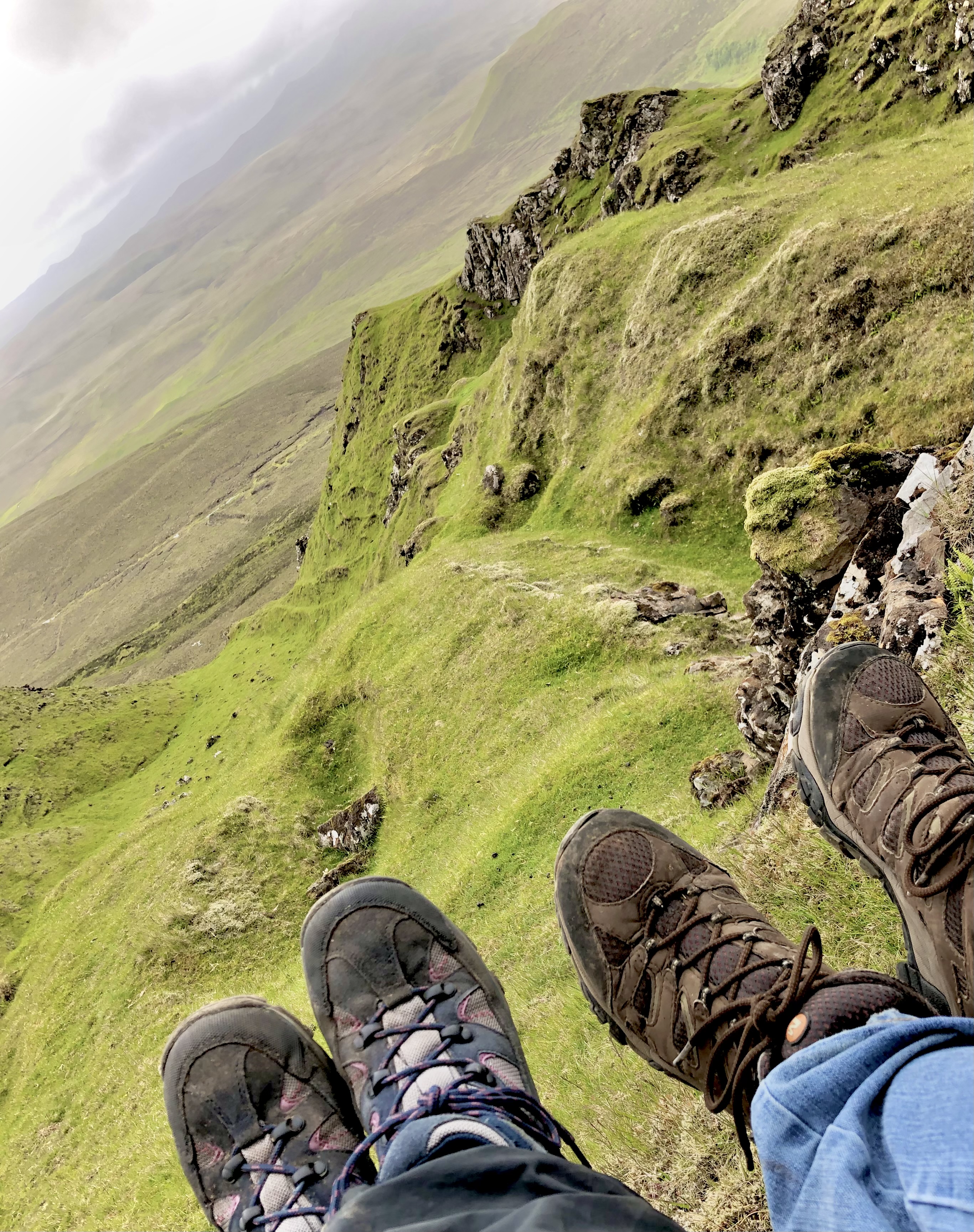 Two people's hiking boots in front of green, jaggedy highlands