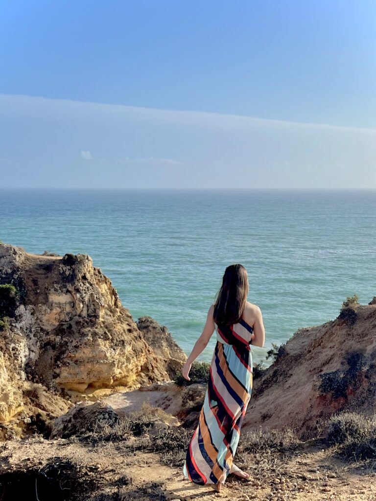 Woman with long dress standing on a golden cliff overlooking the ocean