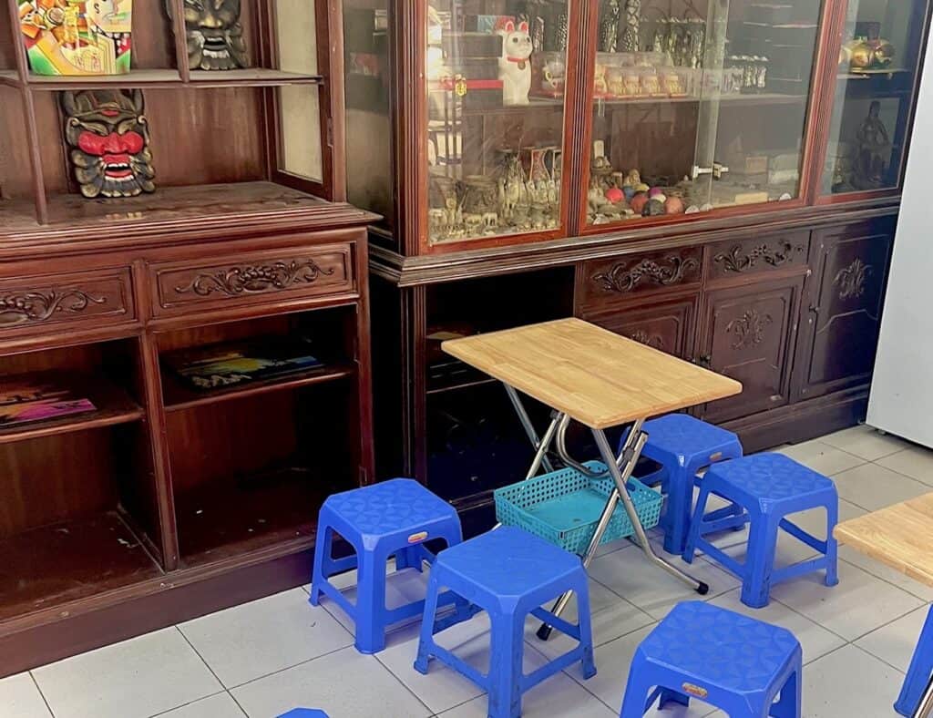 A table with 5 low plastic blue stools surrounding it. The table is in a room with a large china hutch containing various Asian trinkets. 