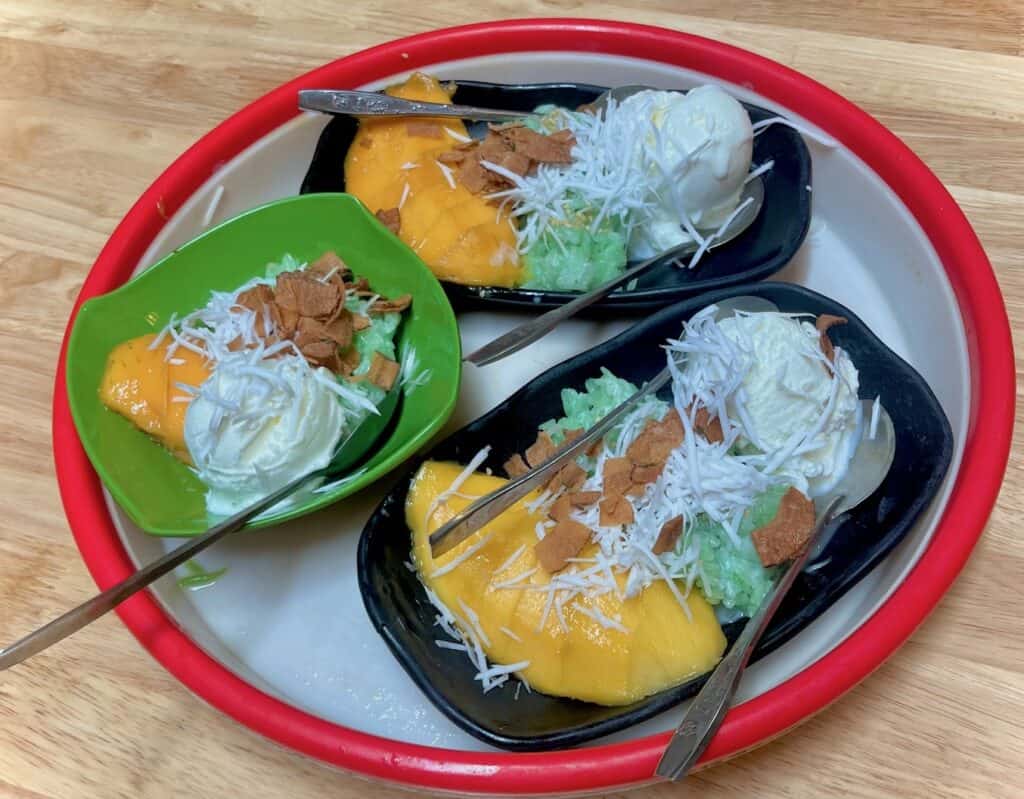 Three bowls of food each containing: light green rice, a ripe sliced mango, and white ice cream with coconut shreds on top.