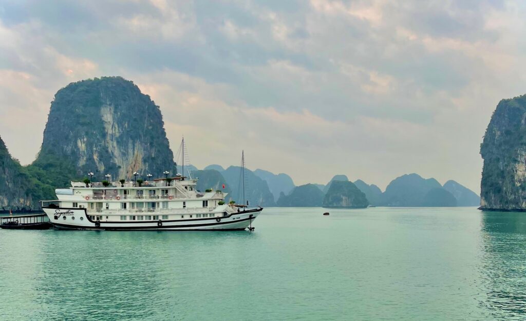 Ship floats in a turquoise bay in Halong Bay with multiple towering limestone islands in the distance