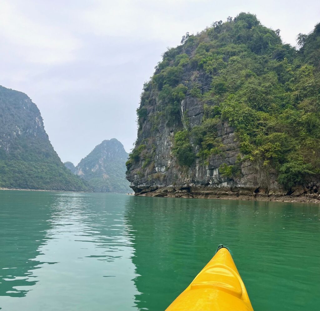 Yellow kayak front is visible floating in green waters with jungle islands in the distance.