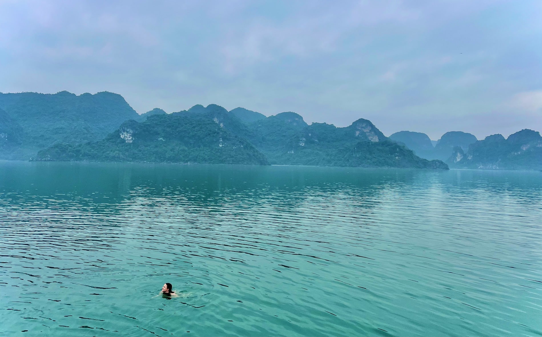 Woman swimming in turquoise waters with towering limestone mountains in the distance