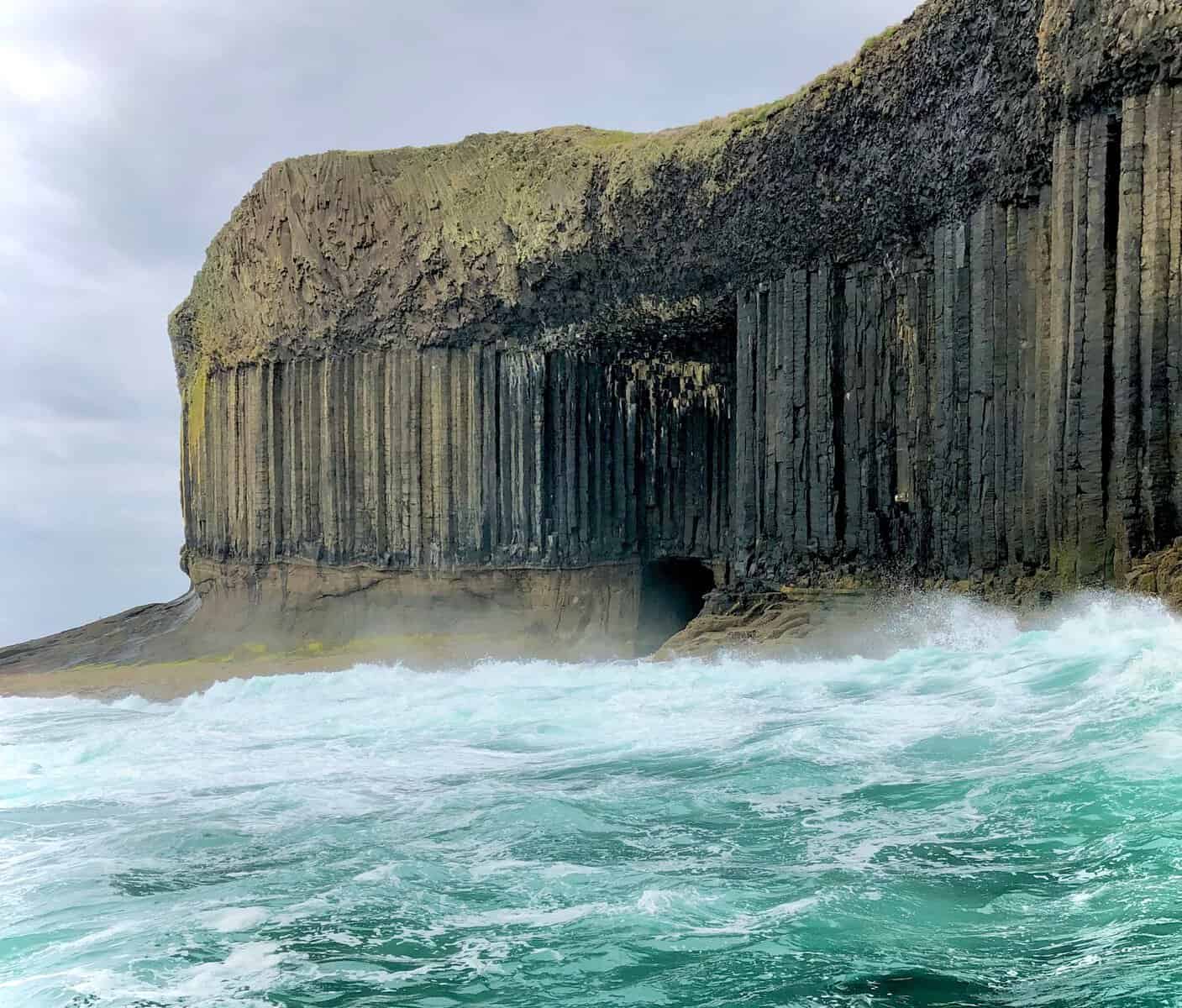 A stunning view of Fingal's Cave on the Isle of Staffa, Scotland, featuring its unique basalt columns and the choppy turquoise sea in the foreground.