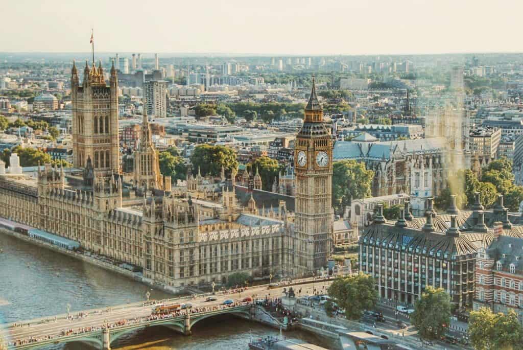 An aerial view of the Palace of Westminster in London, featuring the iconic Big Ben clock tower, the Thames River, and the bustling cityscape in the background.