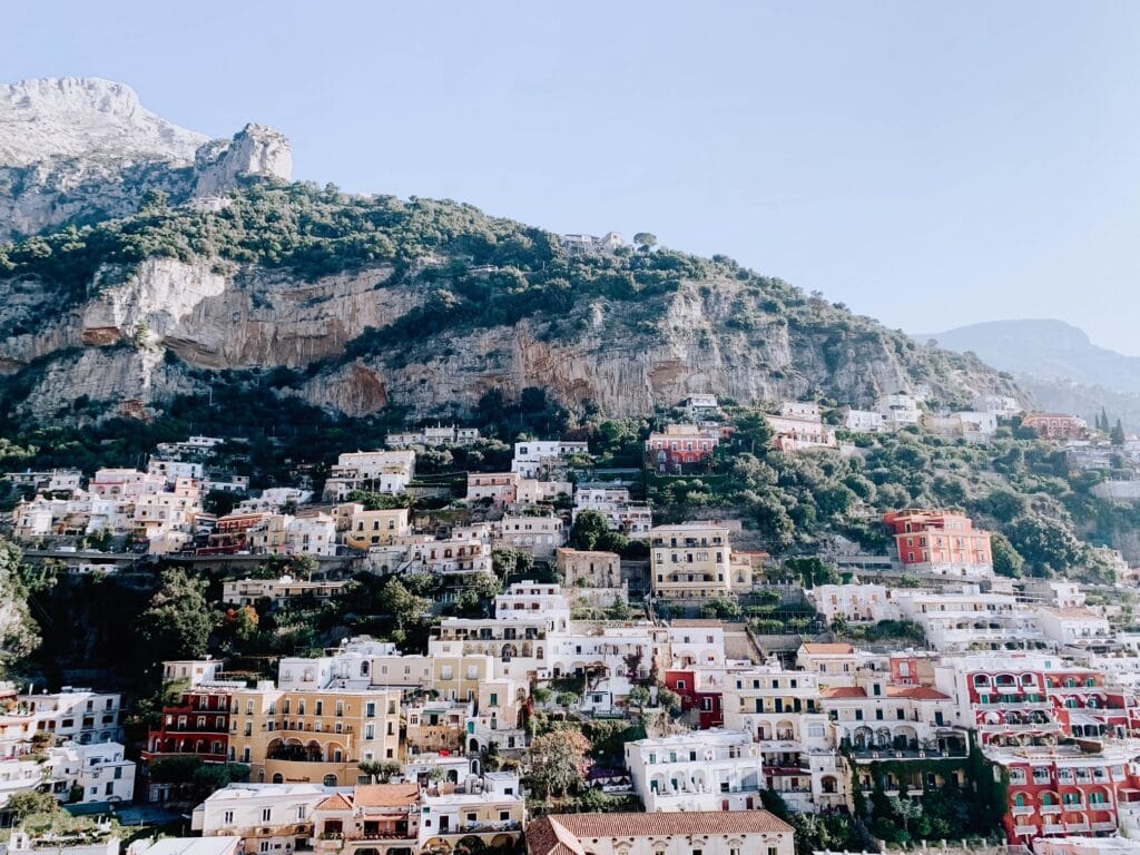 Pastel homes spread around a large green hill. Elevation is one thing to consider when creating an Italy packing list.