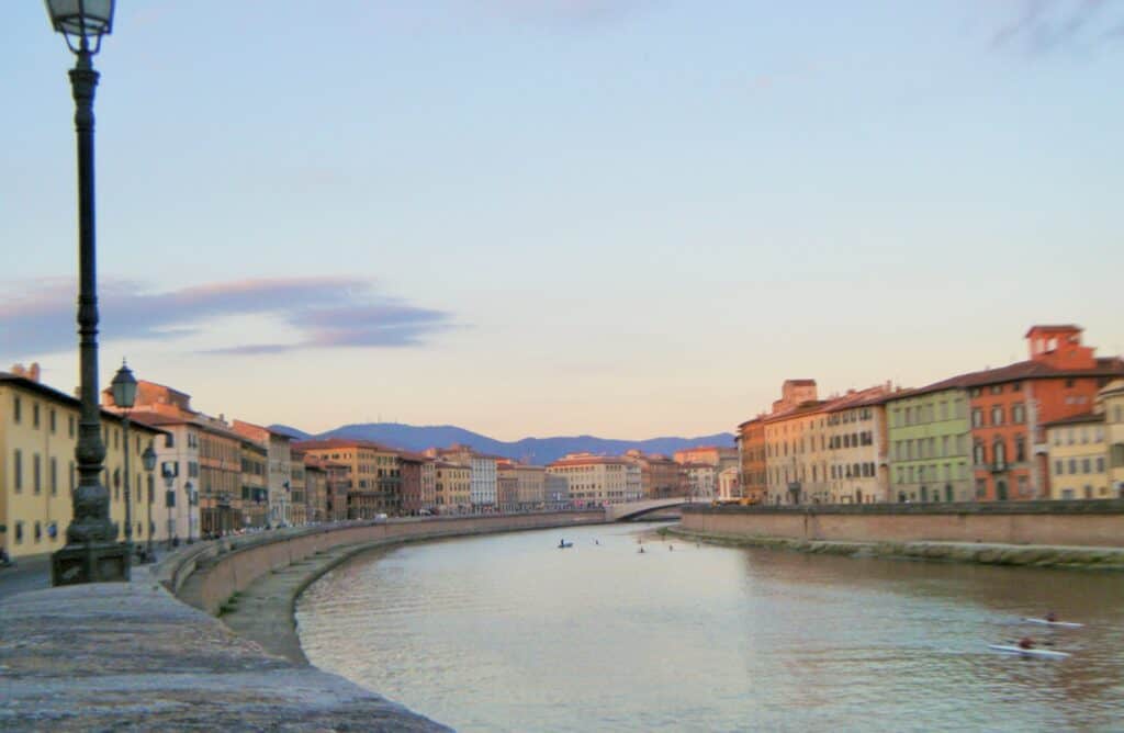 A view of the Arno River running through Pisa with pastel colored Italian homes on each side.