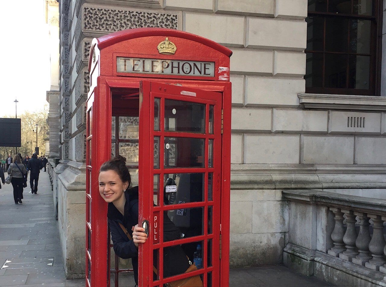 Woman smiles through the open door of a old fashioned red phone booth in London.