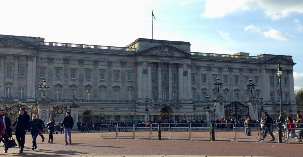 An exterior shot of Buckingham Palace from a distance with dozens of visitors standing behind the gate. Buckingham Palace is a must see on any 2 day London itinerary. 