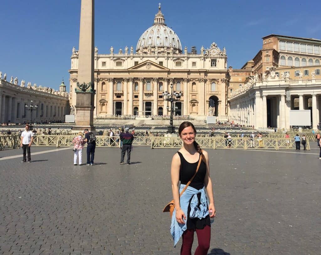 A woman in front of St. Peter's Basicila, keeping her knees covered before entering, one of the most common travel tips for Italy.