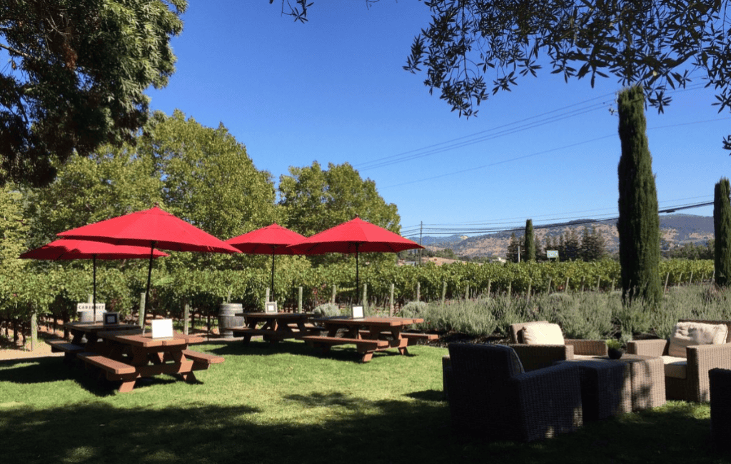 Napa Cellars offers a picnic setting with multiple tables and red umbrellas and patio furniture, making it an Inexpensive Wine tasting in Napa.