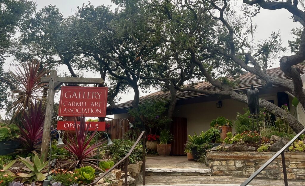 A building surrounding by vegetation with a red wooden sign that reads "Galley Carmel Art Association" this is one of the best things to do in carmel-by-the-sea