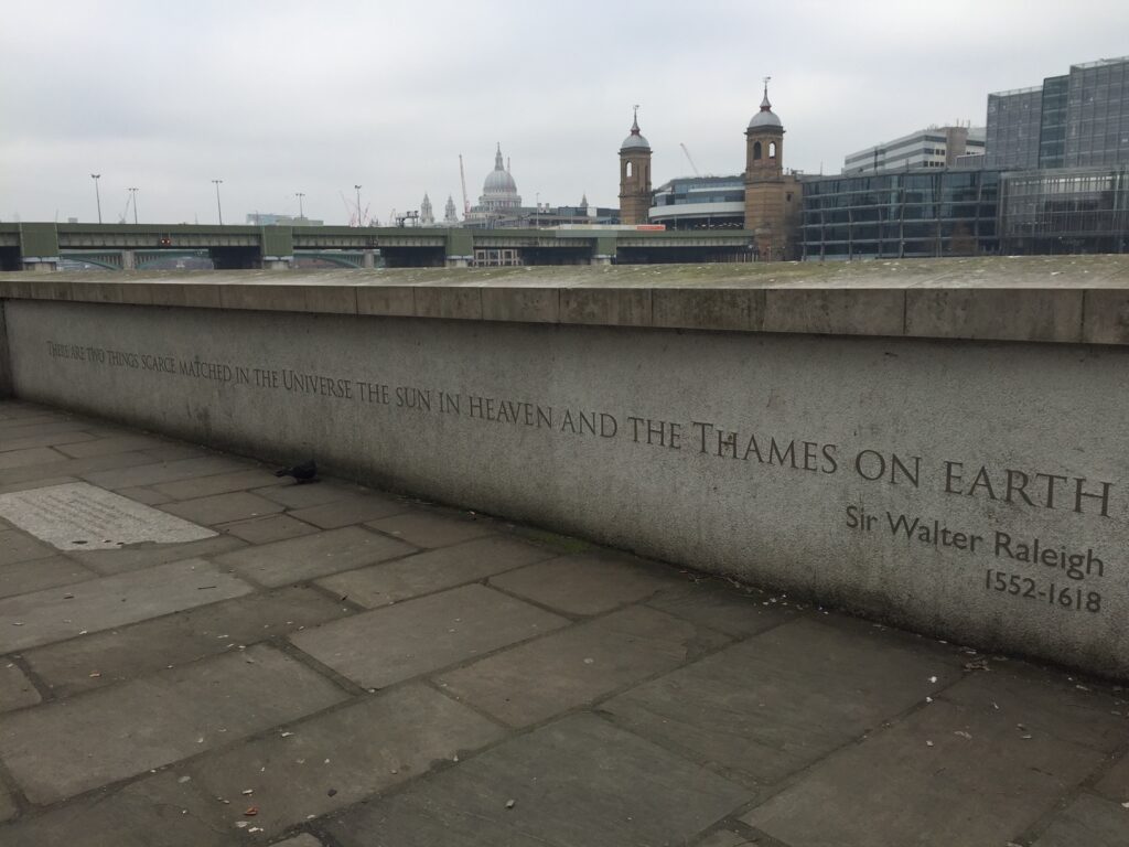 A stone wall featuring a quote from Sir Walter Raleigh reads, "There are two things scarce matched in the Universe, the Sun in Heaven and the Thames on Earth." The backdrop shows a cloudy sky with a river view and distant buildings.